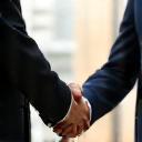 Image representing the completion and handover phase, showing a finished building and a handshake symbolizing successful project completion and client satisfaction.